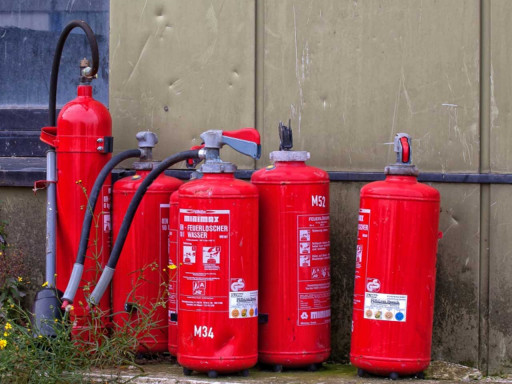 Five red fire extinguishers standing up against the wall.