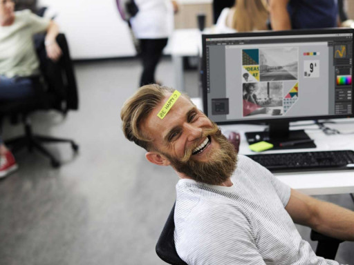 Man sat in a chair smiling with a post it note on his head.